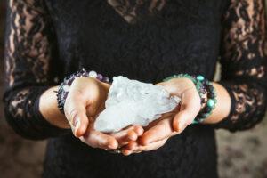 Healer woman holding pure quartz crystal cluster in palms hands.